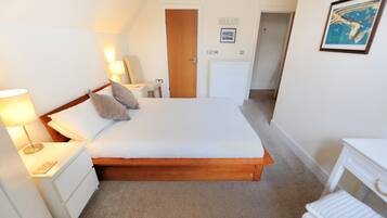 Une chambre à coucher avec un lit en bois, des tables de chevet blanches, une commode, une lampe, une petite chaise et un bureau avec une chaise.