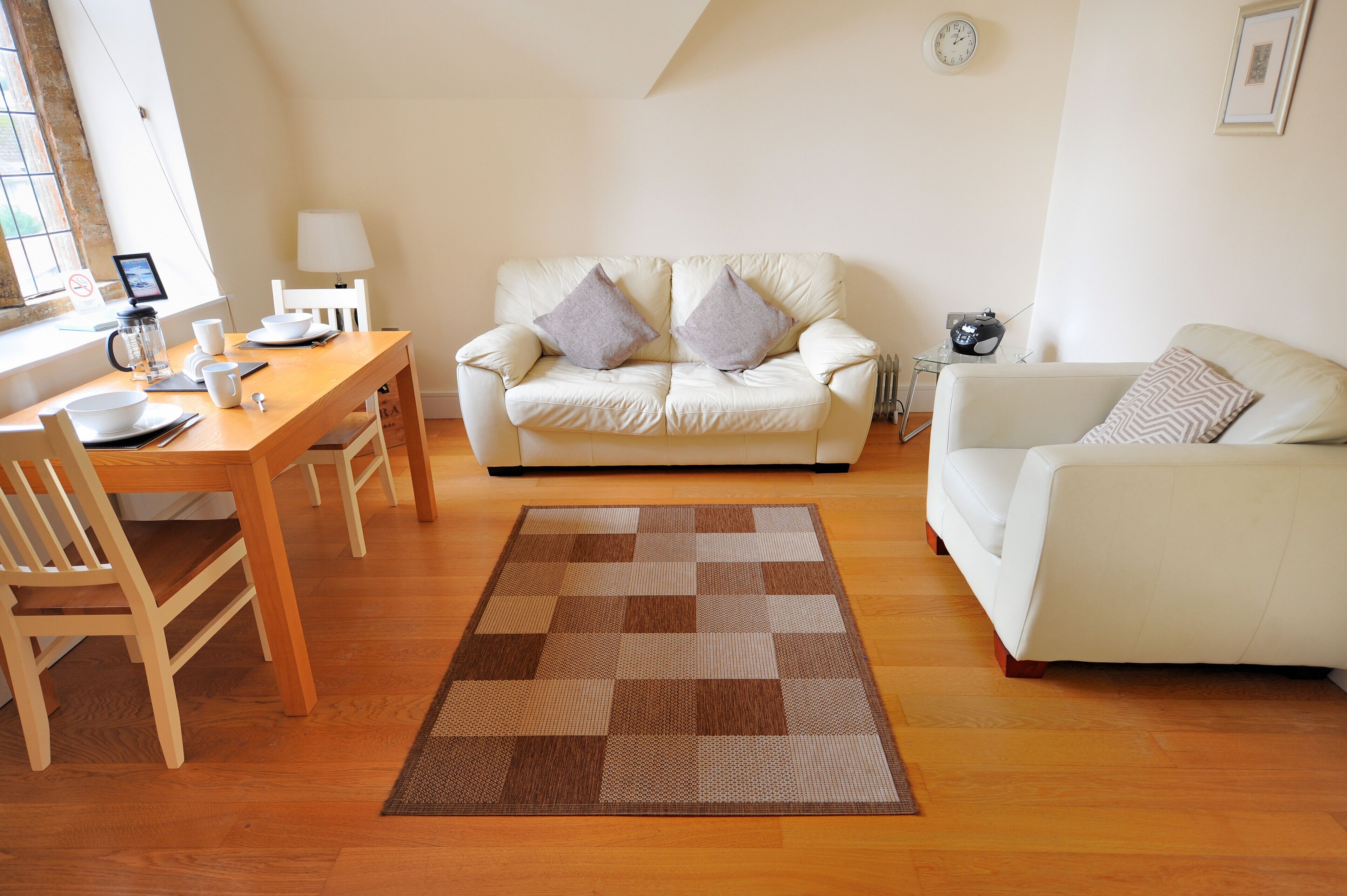 A living room with a wooden dining table, white sofa, and a patterned rug.