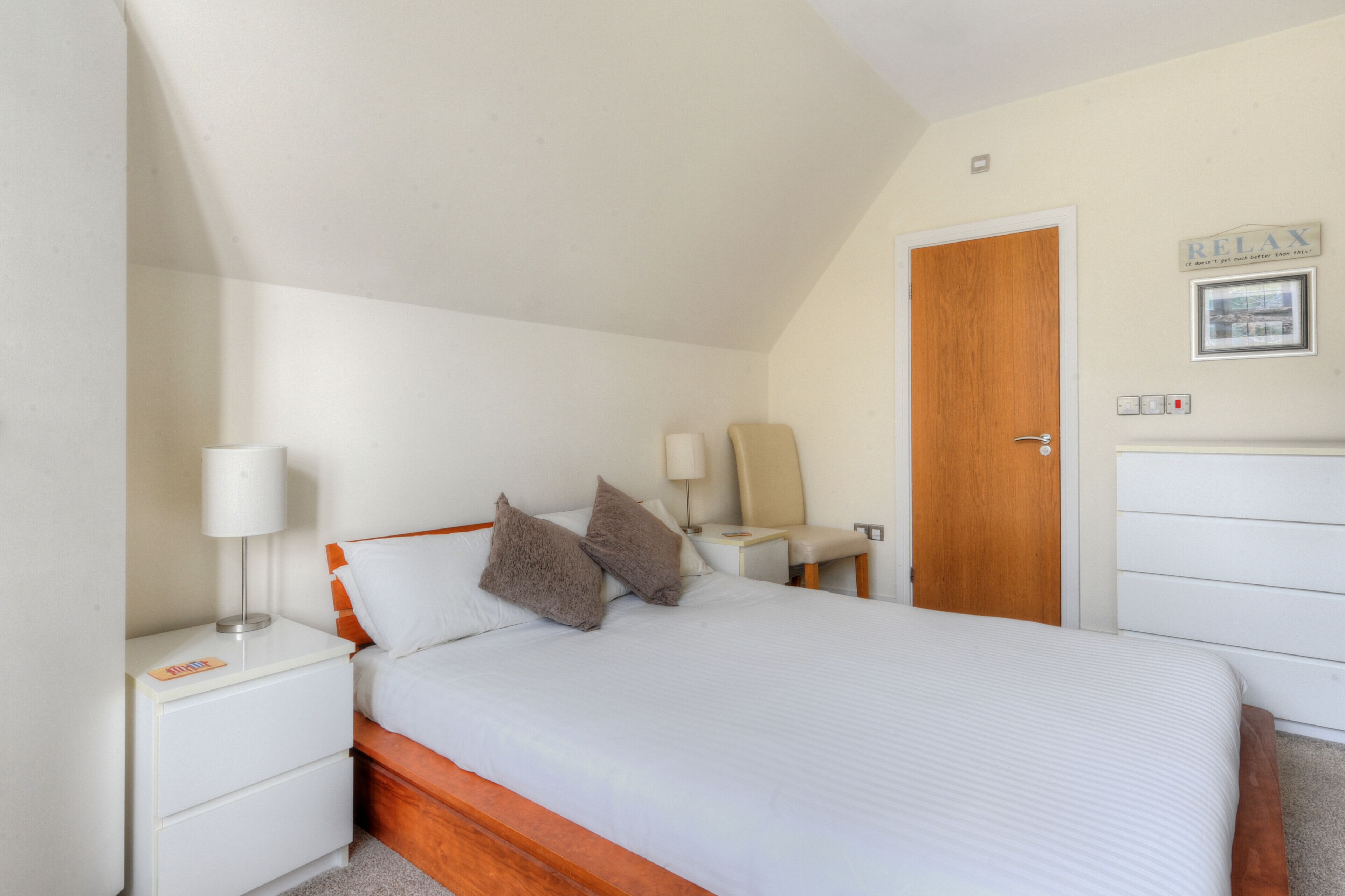 A bedroom with a wooden bed, white nightstands, a wooden door, and a white dresser.