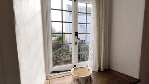 A room with a white door, a window with a view of greenery and buildings, and a floral-patterned bowl on the floor. - Ivy Cottage (Lyme Regis)