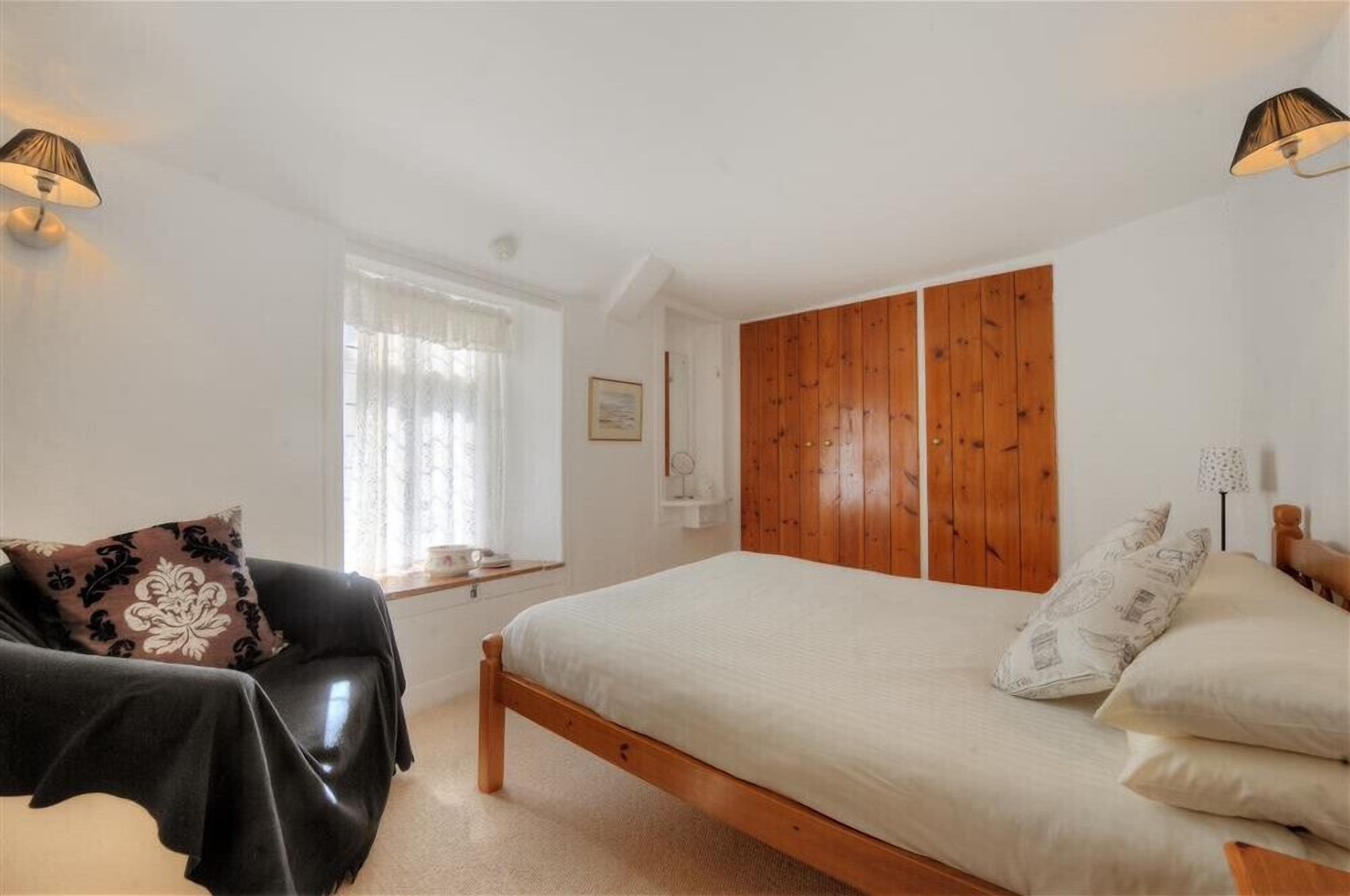 A bedroom with a wooden bed, a black leather chair, and a window with curtains.