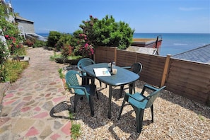 A patio with a table and chairs, a stone pathway, and a view of the sea. - Ross House (Lyme Regis)