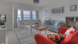 A spacious living room with a large window, a red sofa, a light blue sofa, a wooden coffee table, and a bookshelf. - Ross House (Lyme Regis)