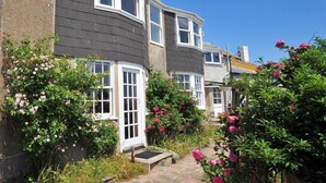 A row of houses with dark grey siding and white trim, surrounded by lush gardens with pink and red flowers. - Ross House (Lyme Regis)