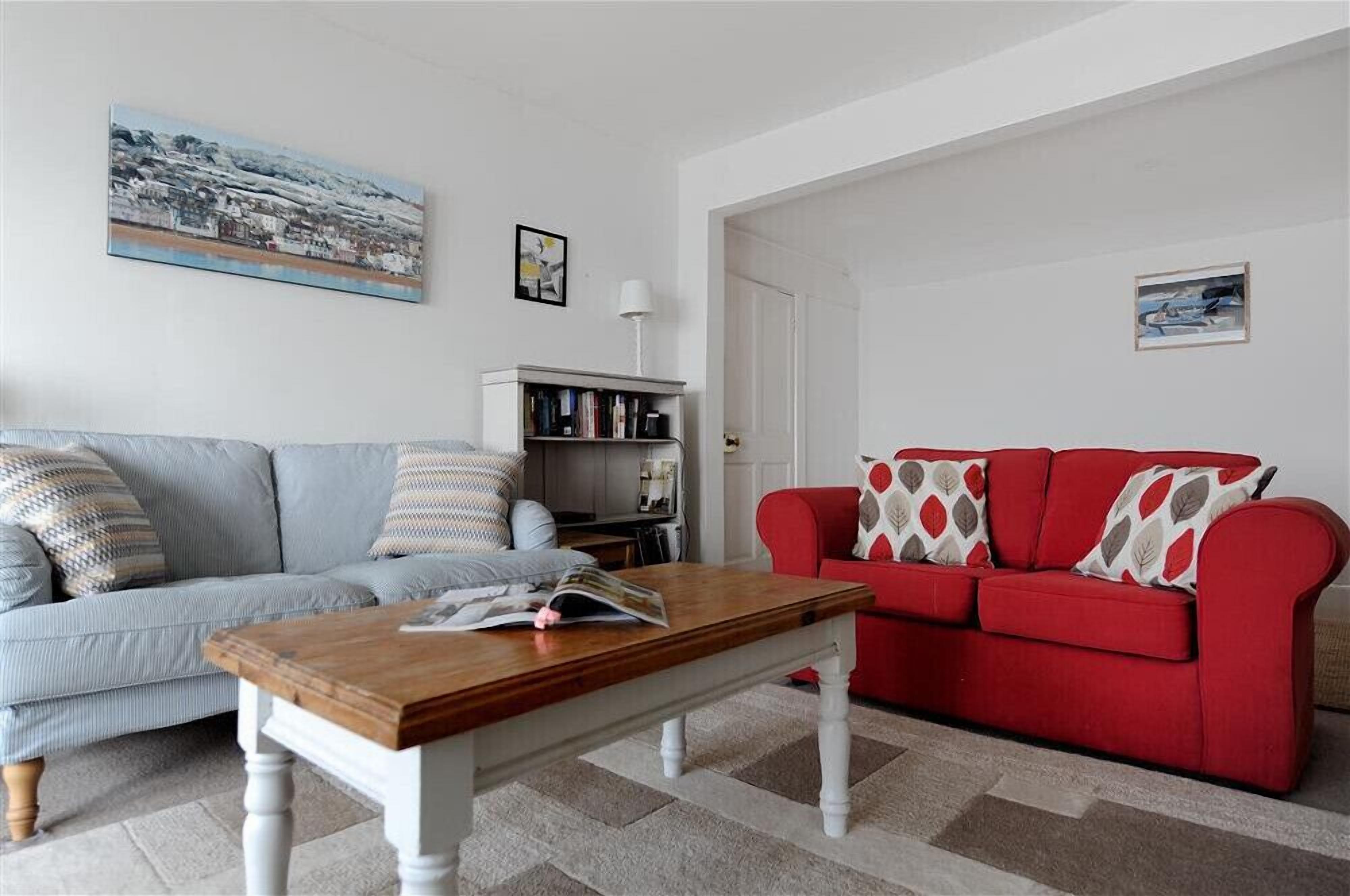A living room with a grey sofa, a red sofa, a wooden coffee table, and a bookshelf.