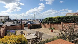 A parking lot with several cars and a white van, surrounded by a brick wall and greenery. - 2 Cobb View (Lyme Regis)