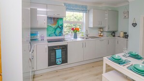 A modern kitchen with white cabinets, a built-in oven, and a window with a view of greenery. - 2 Cobb View (Lyme Regis)