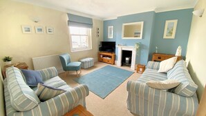 A living room with striped sofas, a blue armchair, a fireplace, and a television. - 2 Cobb View (Lyme Regis)