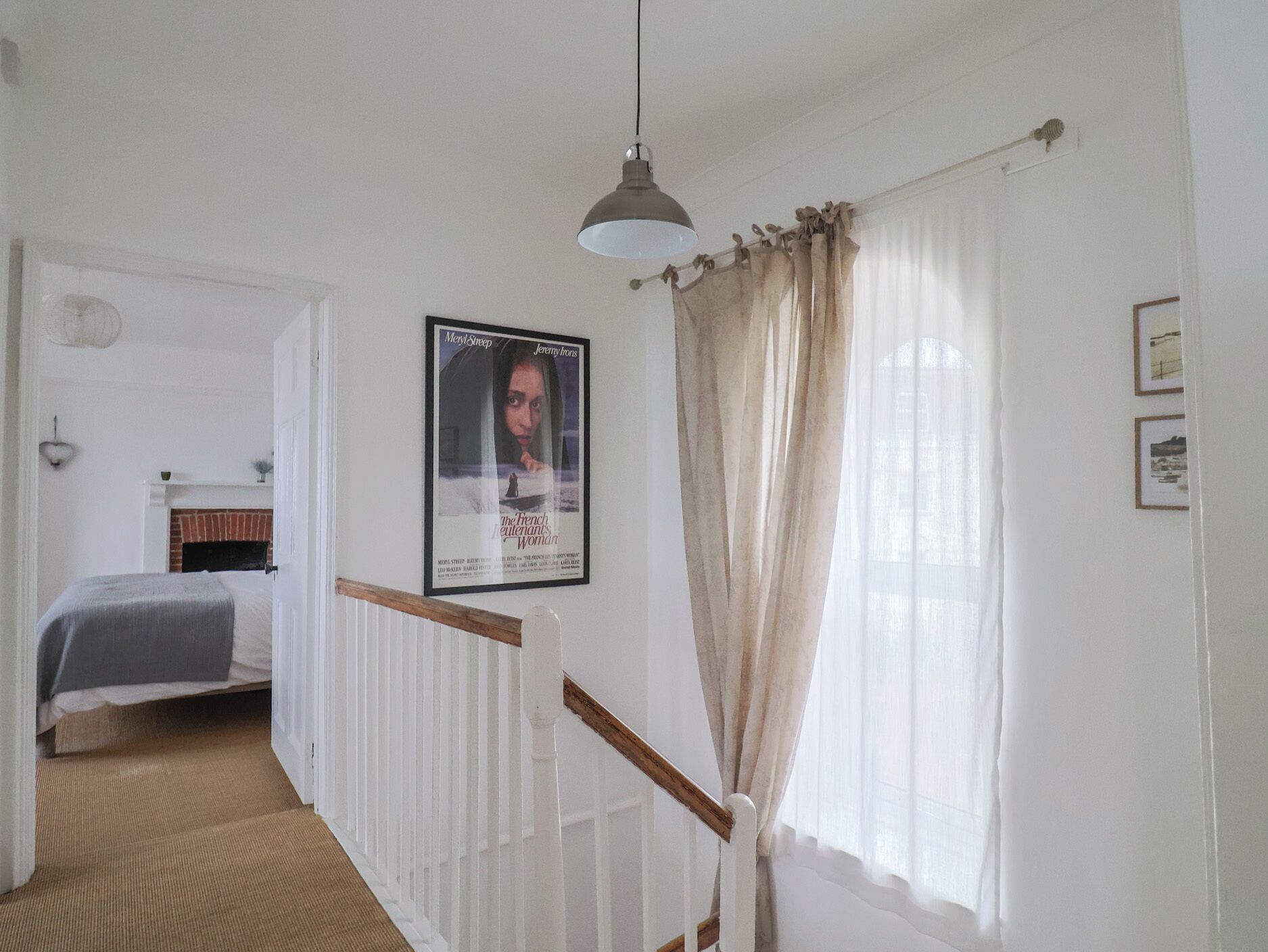 Una camera da letto con un letto, una lampada a sospensione, un quadro e una finestra con tende.