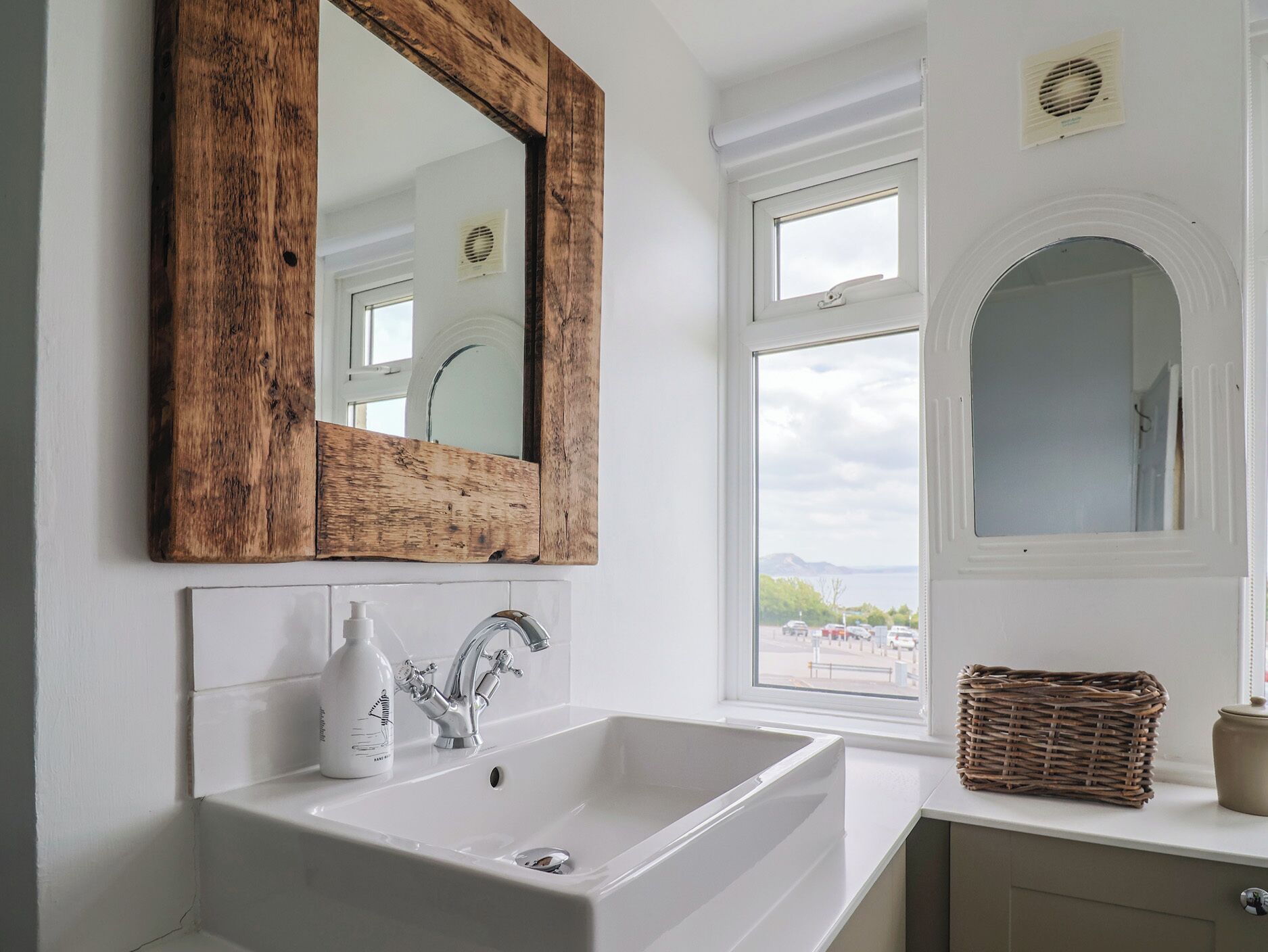 A bathroom with a white sink, a wooden-framed mirror, and a view of a parking lot through a window.