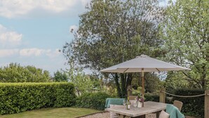 Un patio al aire libre con una mesa y sillas, rodeado de gravilla y un seto.
