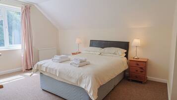 A neatly made bed with folded towels, two bedside lamps, a small wooden nightstand, and a window with curtains.