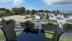Varanda com mesa e cadeiras, com vista para um estacionamento e uma fileira de casas.