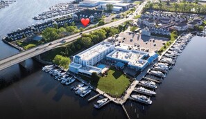 An aerial view of a marina with boats docked, a large building with a blue roof, and a parking lot.