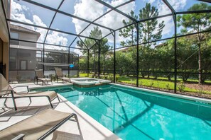 A swimming pool with lounge chairs and a hot tub, surrounded by a glass enclosure with a view of trees and a building.
