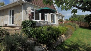A stone house with a green umbrella, a patio, and a well-maintained garden. - Strathaven (Lyme Regis)