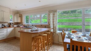 A kitchen with a central island, bar stools, and a dining table set for four. - Strathaven (Lyme Regis)
