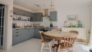 Une cuisine avec des meubles de couleur grise, une table ronde en bois et des chaises blanches.