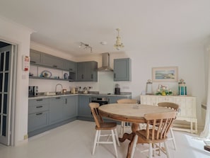A kitchen with grey cabinets, a round wooden table, and white chairs. - 1 Bay View Court (Lyme Regis)