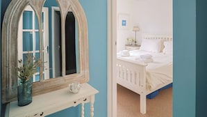 Une chambre à coucher avec un lit, une table de chevet ornée d’un vase, un miroir et une porte donnant sur une autre pièce.