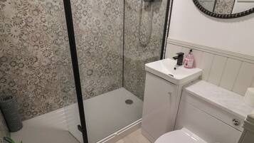 Un baño con ducha, inodoro, lavamanos y espejo.
