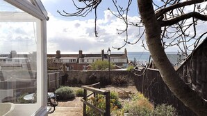 A view from a window overlooking a garden with a wooden deck, a stone wall, and a view of houses across the water.
