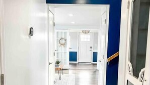 Un pasillo con suelo de madera y paredes blancas que conduce a una habitación con una pared azul decorativa y una puerta con paneles de vidrio.