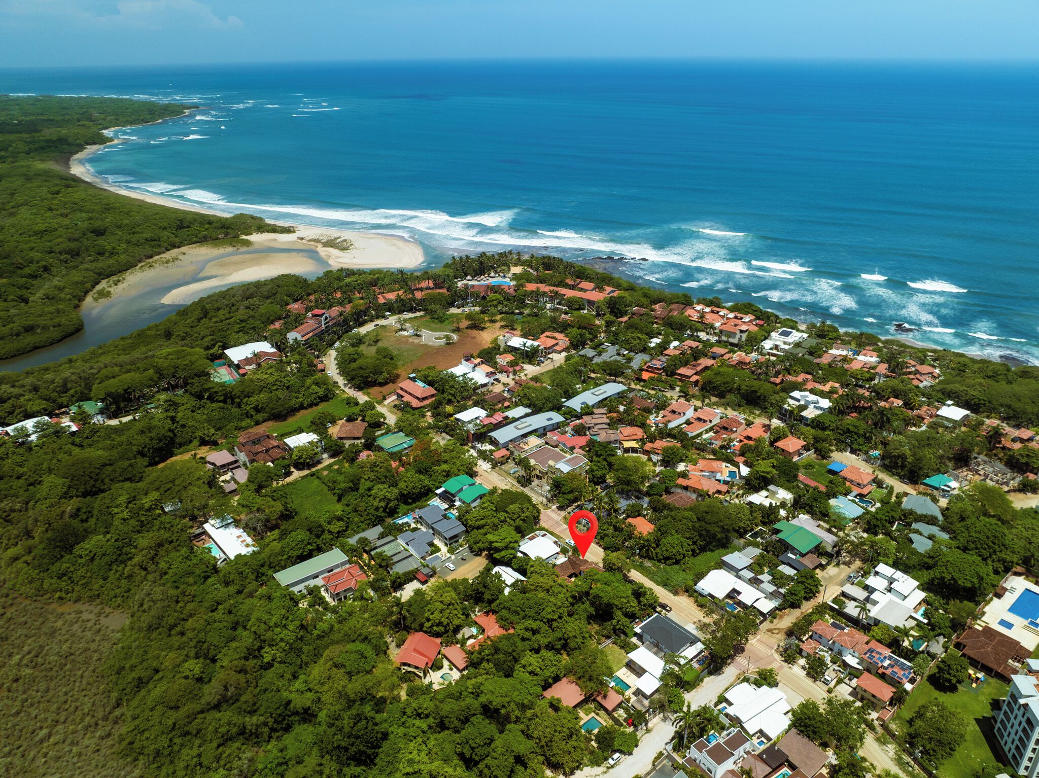 An aerial view of a coastal residential area with houses, a beach, and a river.
