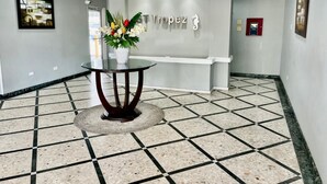 Un área de recepción con mostrador, un florero con flores, un cuadro en la pared y suelo de baldosas.