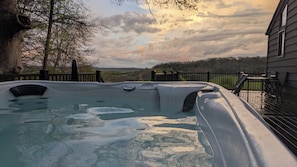 A hot tub with a wooden deck and a view of the landscape.