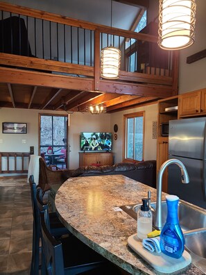 Enjoy cooking in this well-equipped kitchen with a large island countertop, stainless steel sink, and mounted TV.