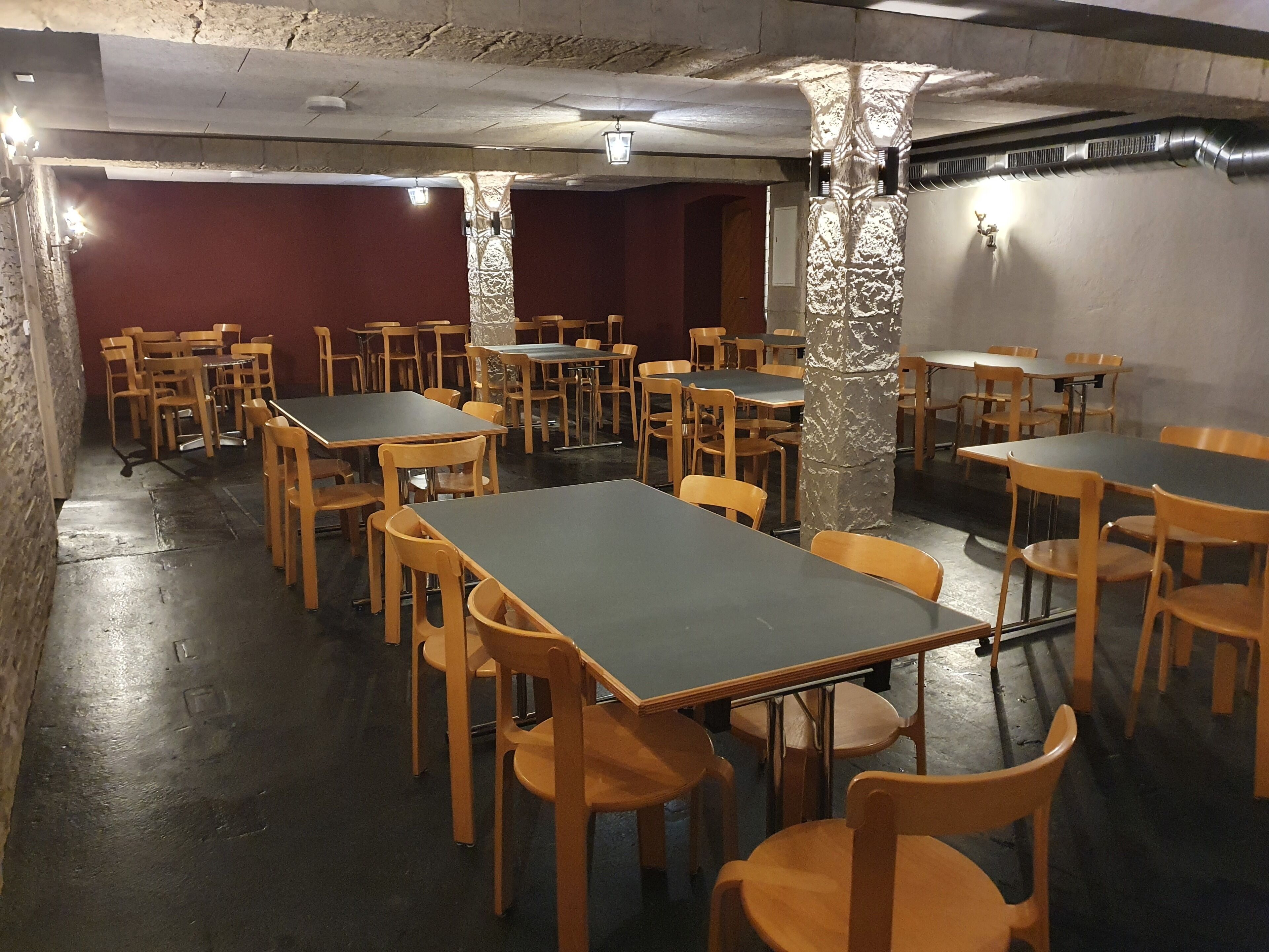 A room with tables and chairs arranged in a grid pattern, with a stone pillar in the center.