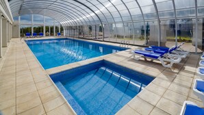 An indoor swimming pool with a glass ceiling, blue lounge chairs, and a tiled floor. - La Recova Hotel & Spa (La Punta)