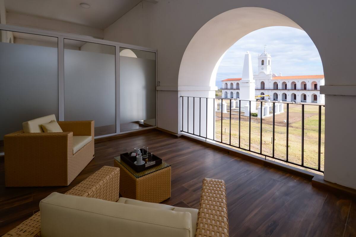 A spacious balcony with a view of a white building with a bell tower.