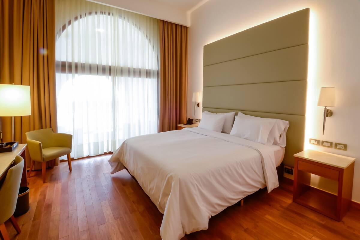 A hotel room with a large bed, a desk, a chair, and a window with curtains.