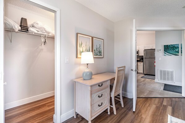 A room with a desk, chair, and a lamp. There is a closet with hanging clothes and a shelf with towels. A kitchen is visible in the background. - Water view and renovated (Melbourne)