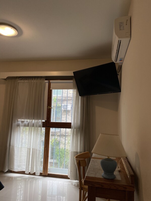 Um quarto com uma mesa de jantar, uma cadeira, uma janela com cortinas e um ar condicionado fixado na parede.