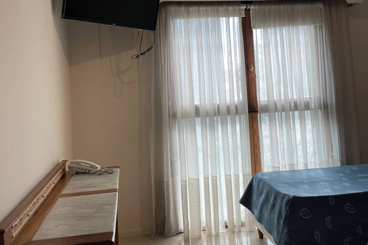 Habitación de hotel con cama, escritorio, teléfono, televisor montado en la pared y aire acondicionado.