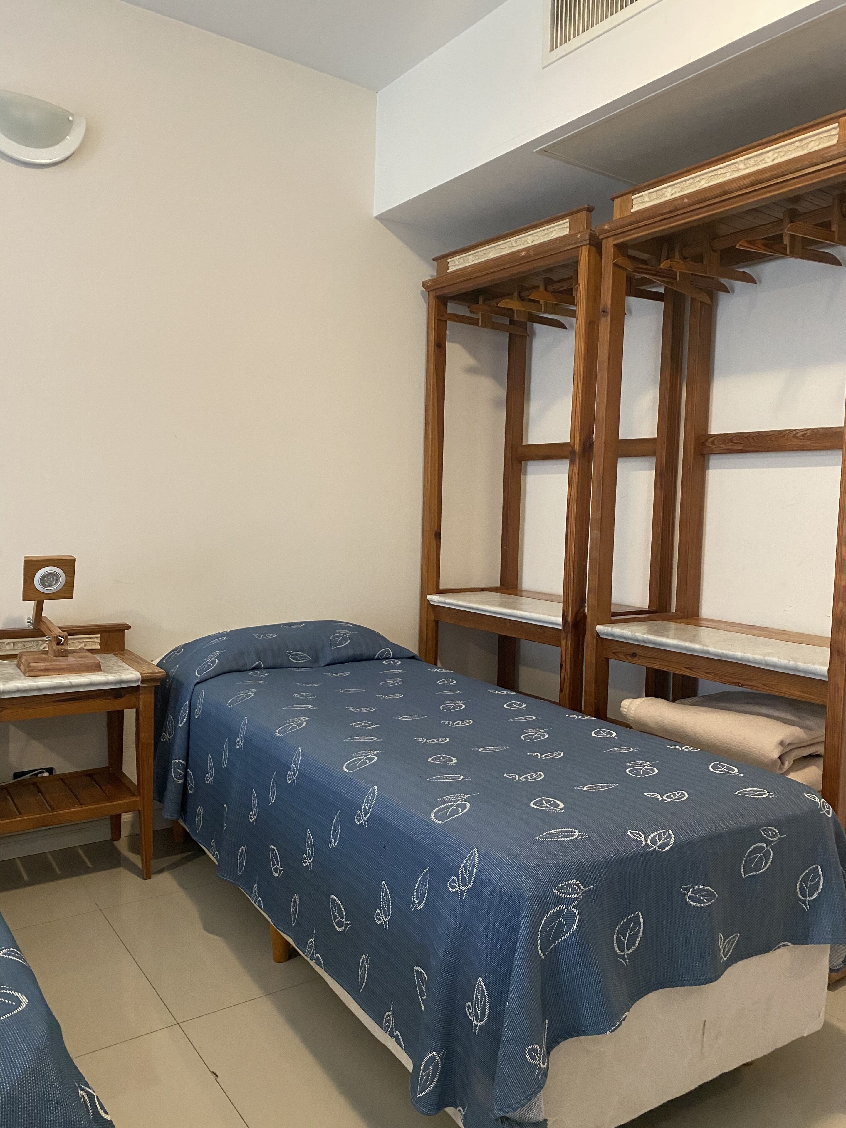 A room with two bunk beds, a small wooden desk with a lamp, and a bed with a blue leaf-patterned bedspread.