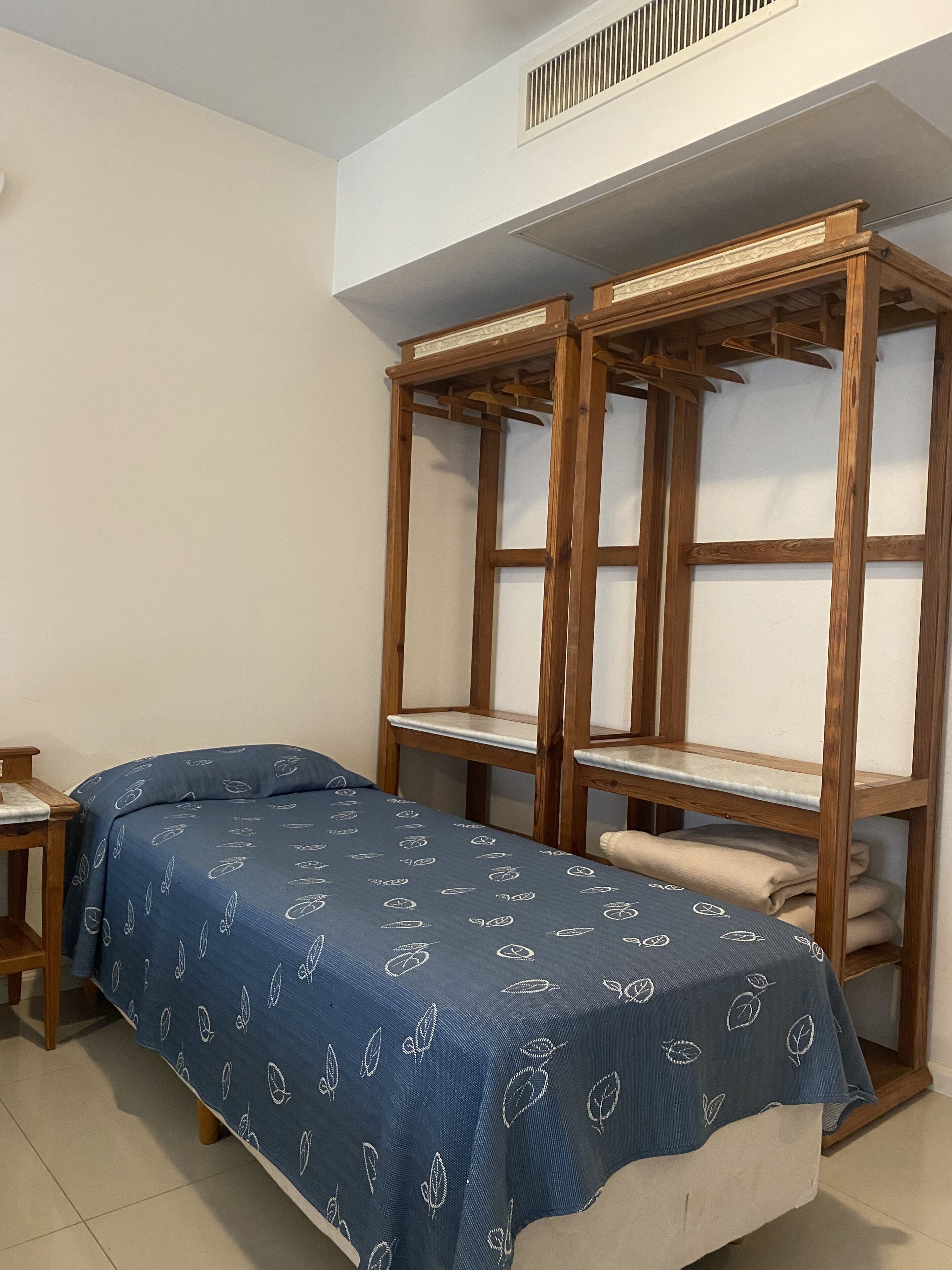 Una habitación con una cama individual, un armario de madera y una mesita.