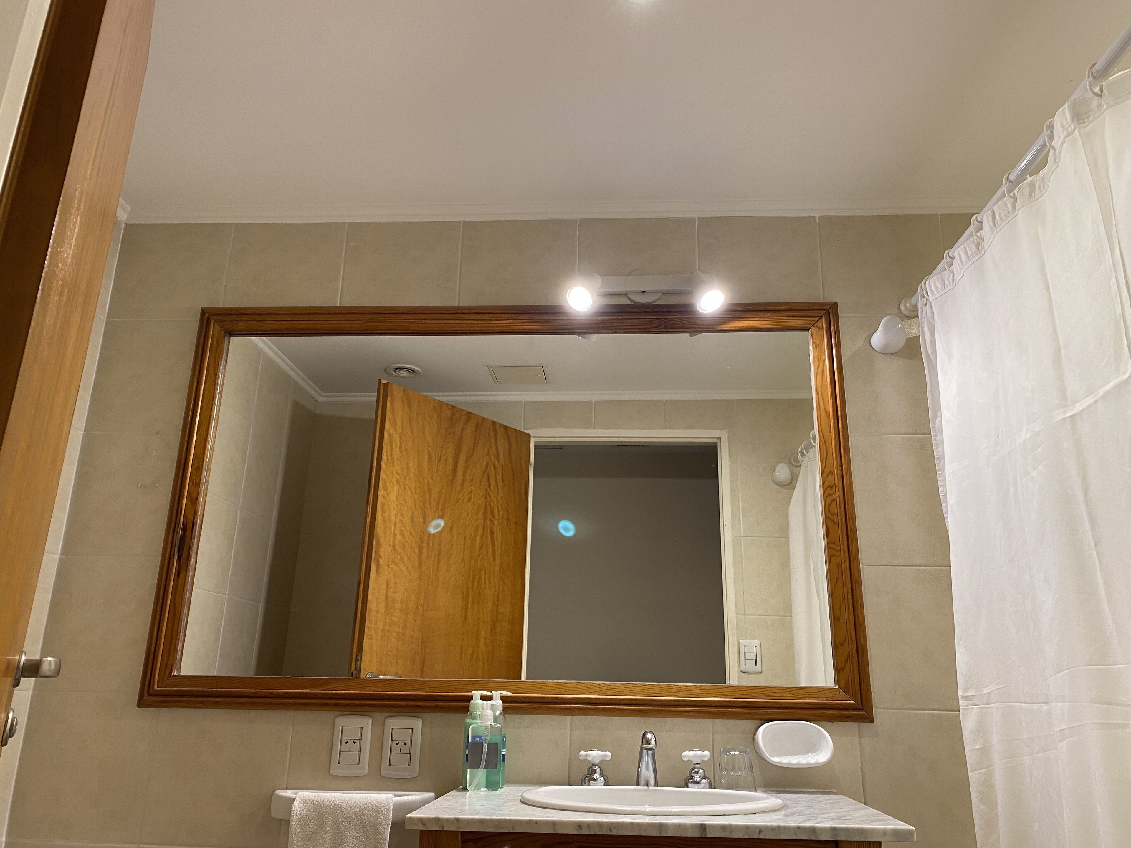A bathroom with a large mirror, a sink, and a shower curtain.