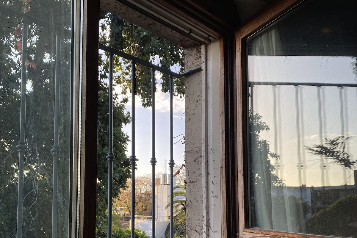 Una ventana con barrotes de metal, un marco de madera y una cortina blanca.