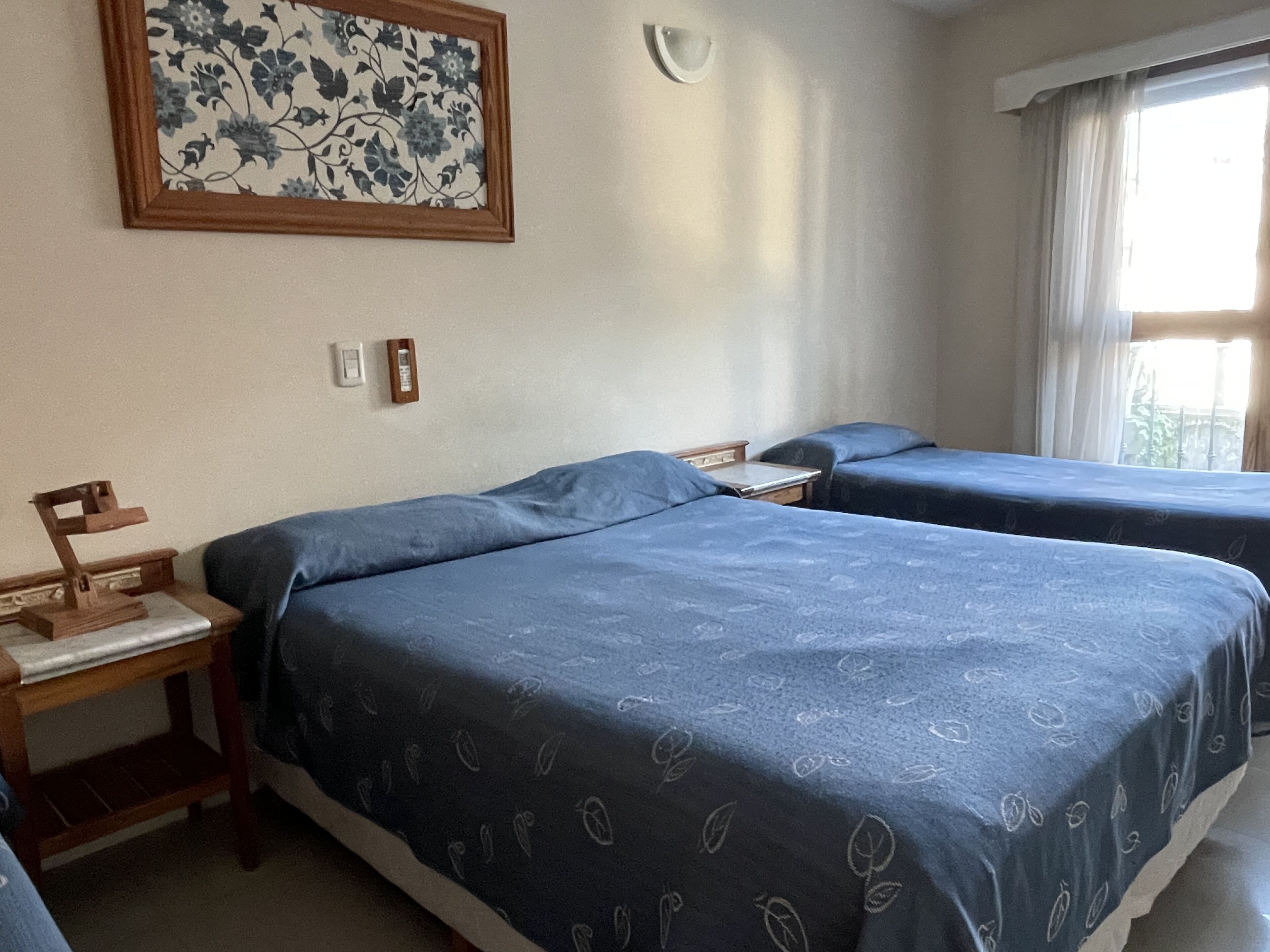 Une chambre avec deux lits, une table de chevet en bois, une horloge murale et un tableau floral encadré.