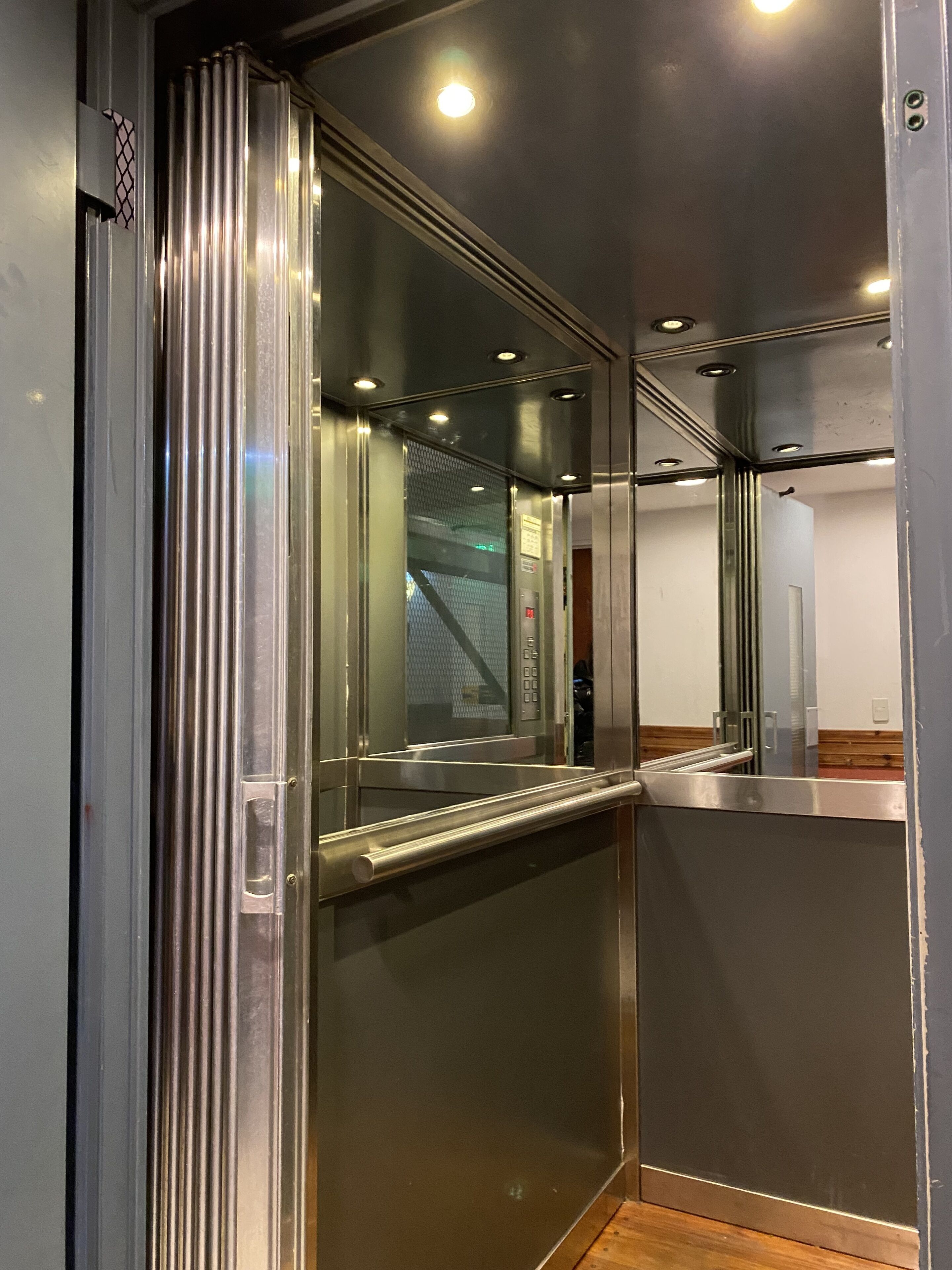 Interior moderno de ascensor con paredes metálicas y un panel de vidrio.