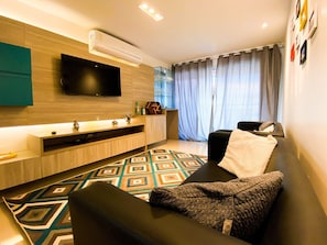 A modern living room with a flat-screen TV, a sofa, a coffee table, and a patterned rug.