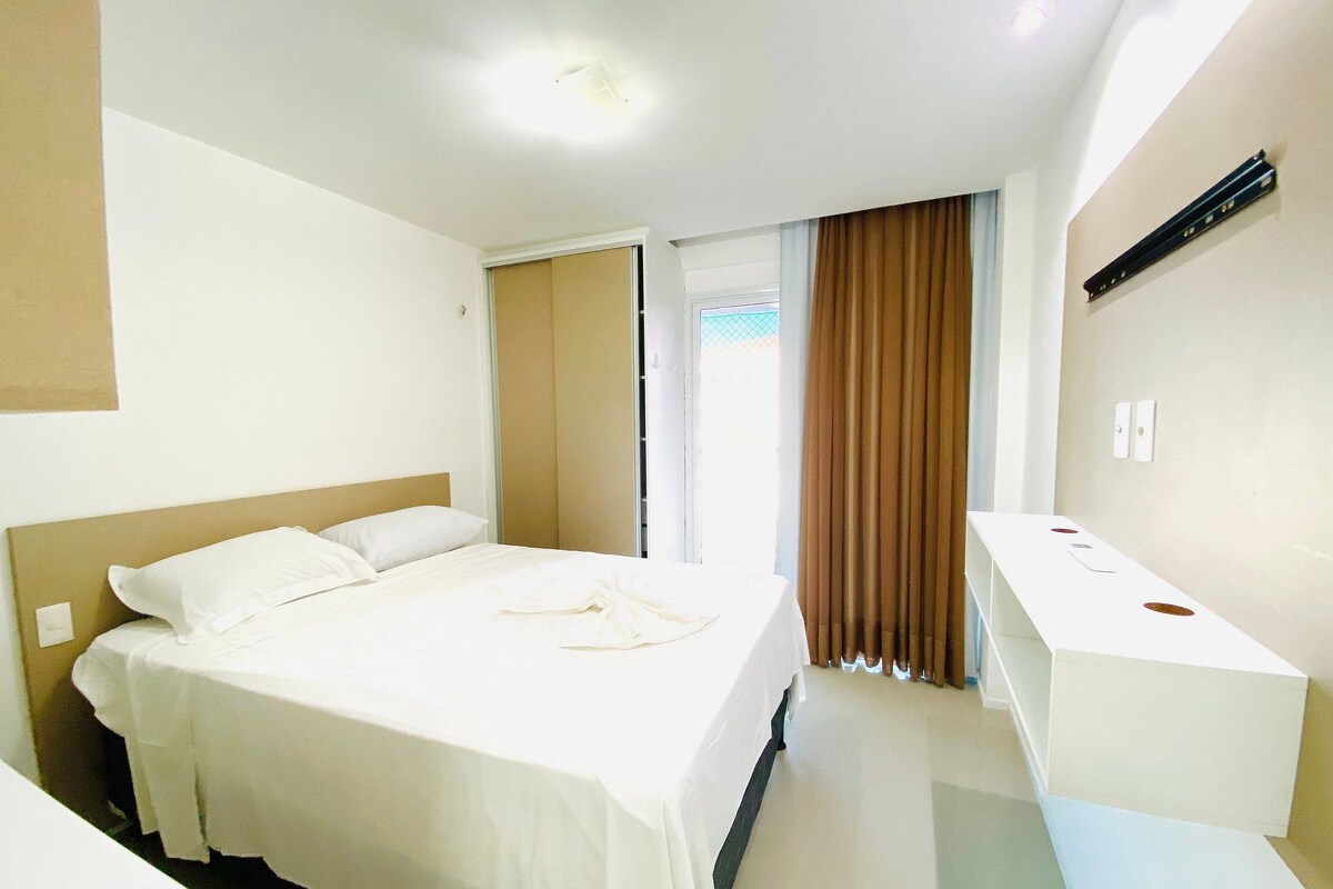 Una habitación de hotel con cama, escritorio, espejo y ventana con cortinas.