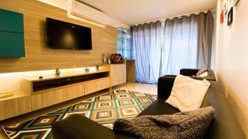 Uma sala de estar moderna com uma TV de tela plana, um sofá, uma mesa de centro e um tapete estampado.