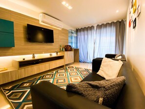 Ein modernes Wohnzimmer mit Flachbildfernseher, einer Couch, einem Couchtisch und einem gemusterten Teppich.