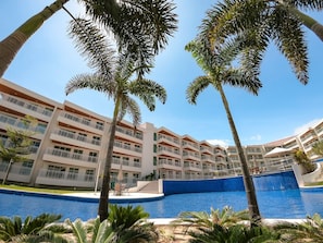 A multi-story hotel with balconies, a swimming pool, and palm trees.