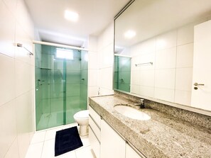 Un baño con cabina de ducha de vidrio, un inodoro blanco, un lavamanos con encimera de granito y un espejo grande.